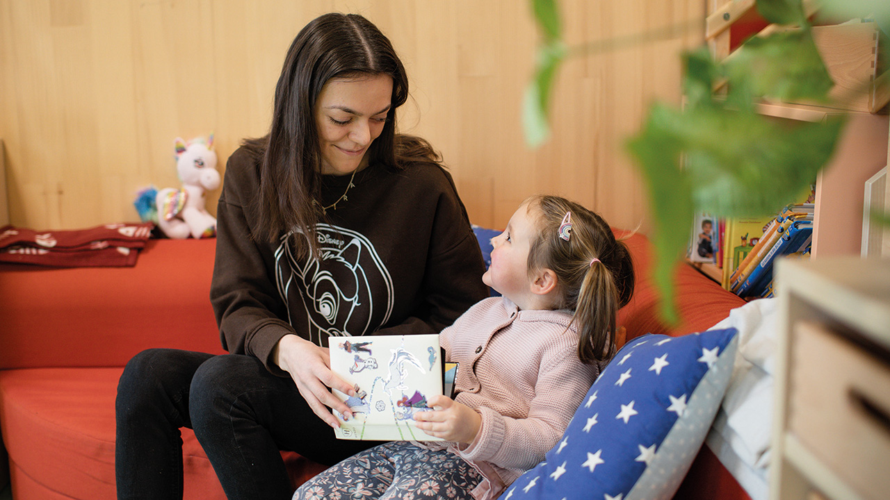 Erziehrin sitzt mit Kind in einer Kuschelecke und liest etwas