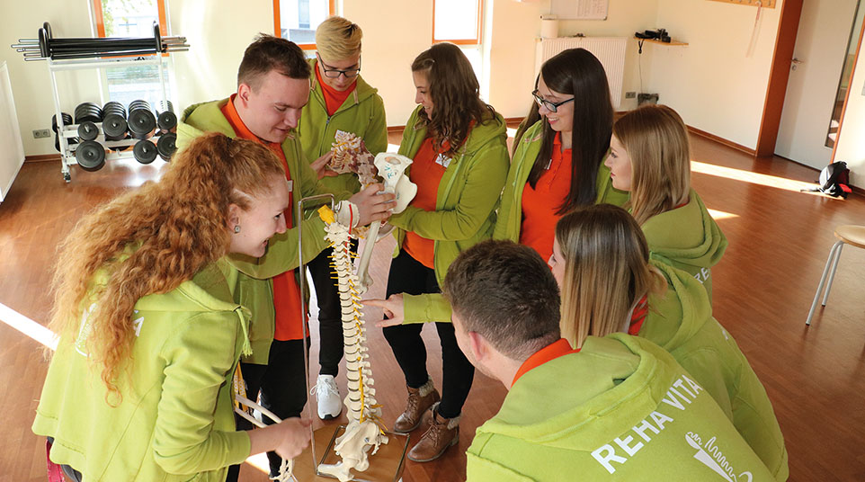 Jugendliche in grünen Shirt stehen um ein Wirbelsäulen-Modell herum und erklären sich gegenseitig etwas