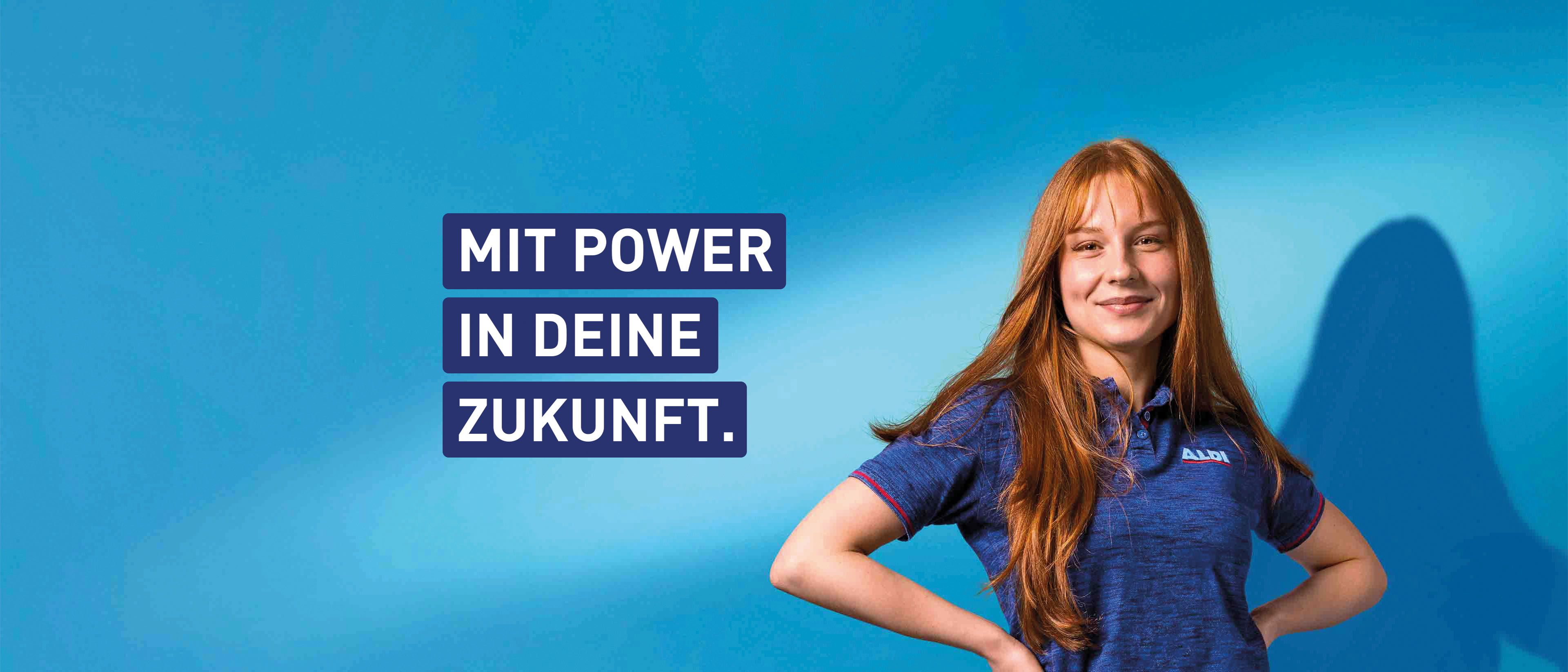 Eine Person in blauem T-Shirt steht vor einem blauen Hintergrund, lächelt und wirkt selbstbewusst. Daneben steht der Slogan: MIT POWER IN DEINE ZUKUNFT