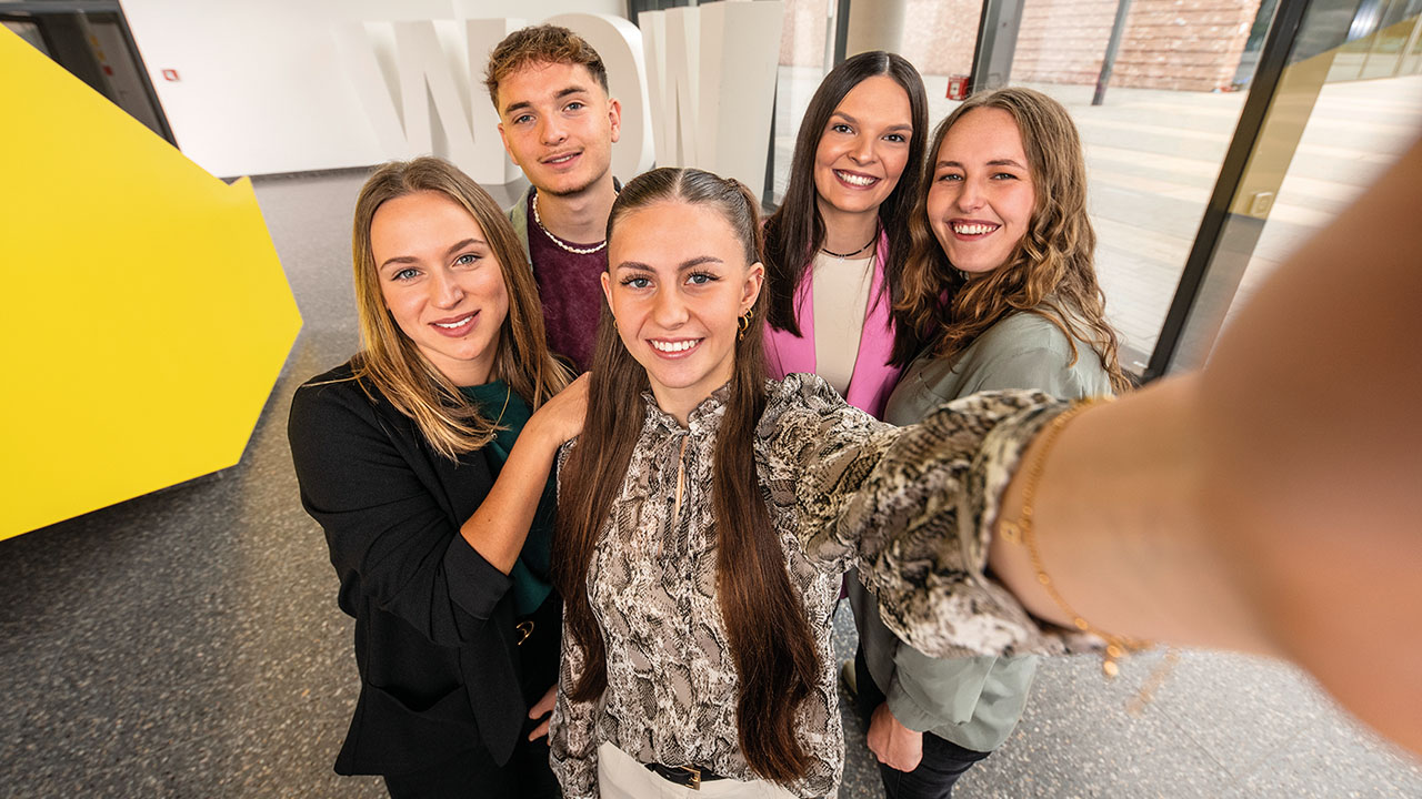 Fünf Personen machen ein Selfie und lächeln in die Kamera.