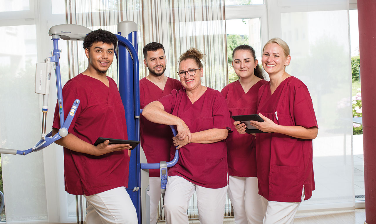 Gruppenbild von Pflegekräften in weinroten Kittel und weißer Hose