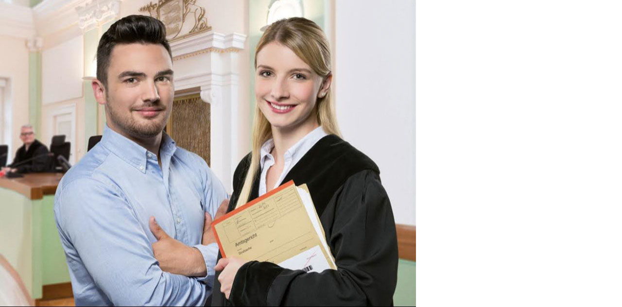 Zwei Personen lächeln in die Kamera im Hintergrund ist ein Gerichtssaal zu sehen.