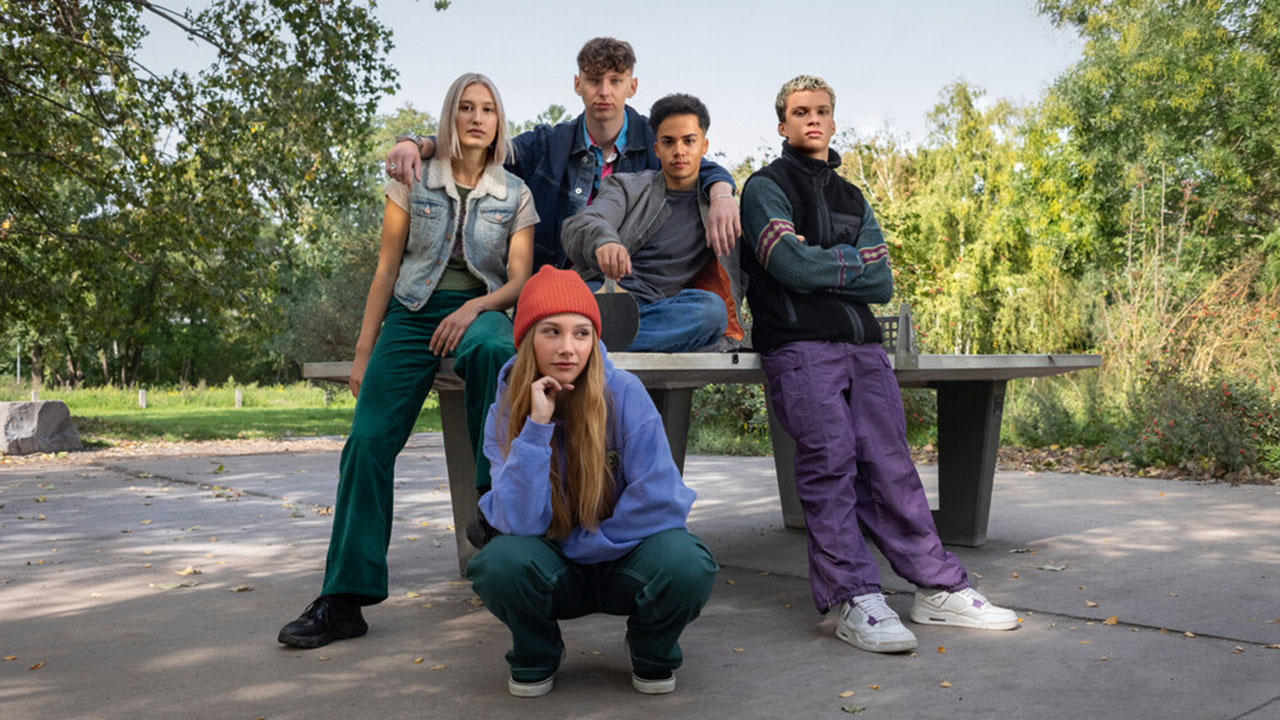 Fünf junge Personen sitzen auf und lehnen an einer Tischtennisplatte im Grünen