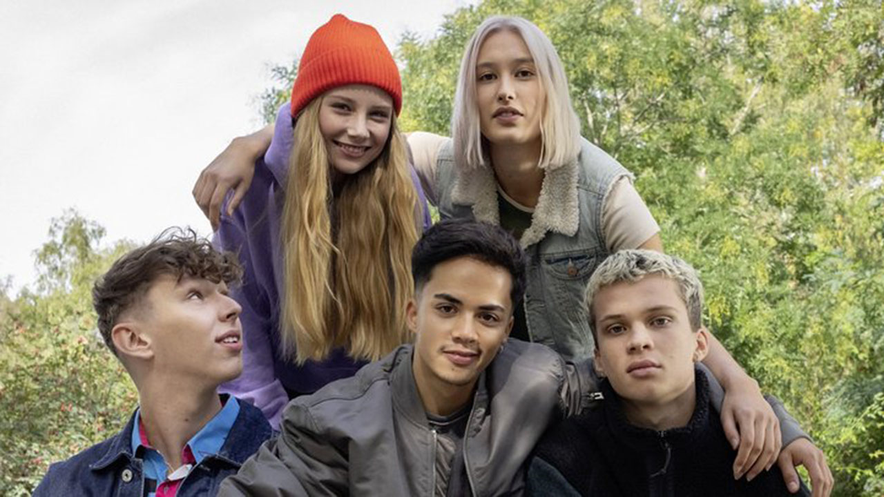 Fünf junge Menschen Arm in Arm, im Hintergrund grüne Bäume