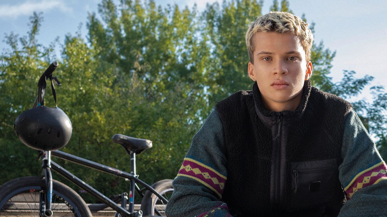 Junger Mensch sitzt neben seinem Fahrrad und schaut in die Kamera