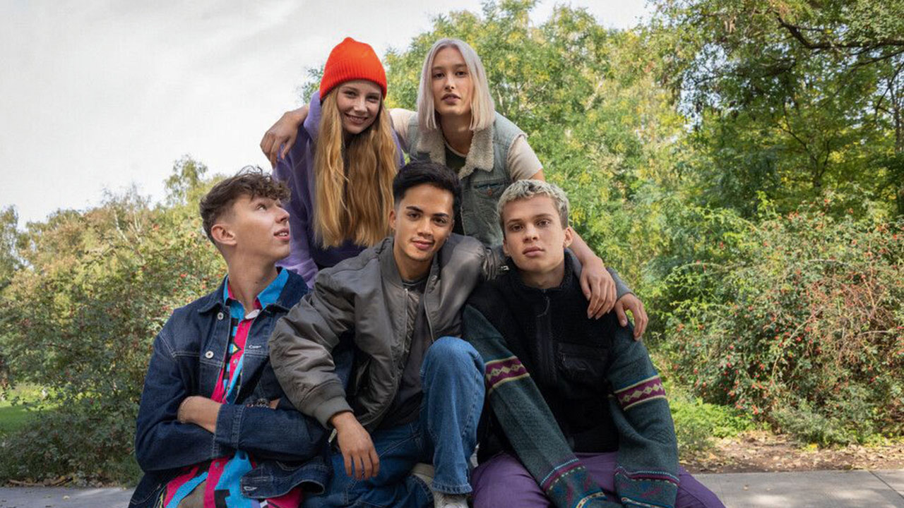 Fünf junge Personen sitzen auf und lehnen an einer Tischtennisplatte im Grünen