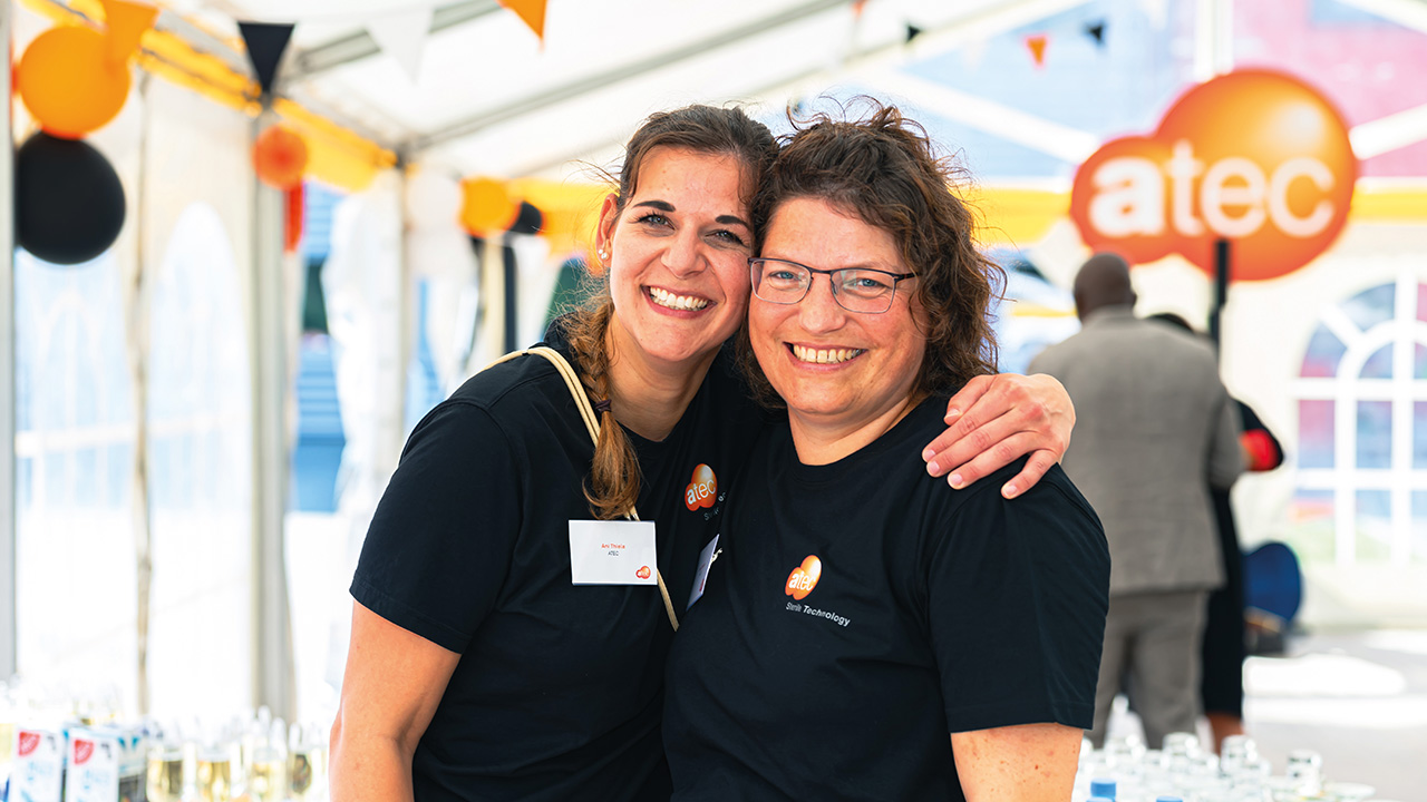 Zwei Mitarbeiterinnen von ATEC stehen Arm in Arm und lachen in die Kamera