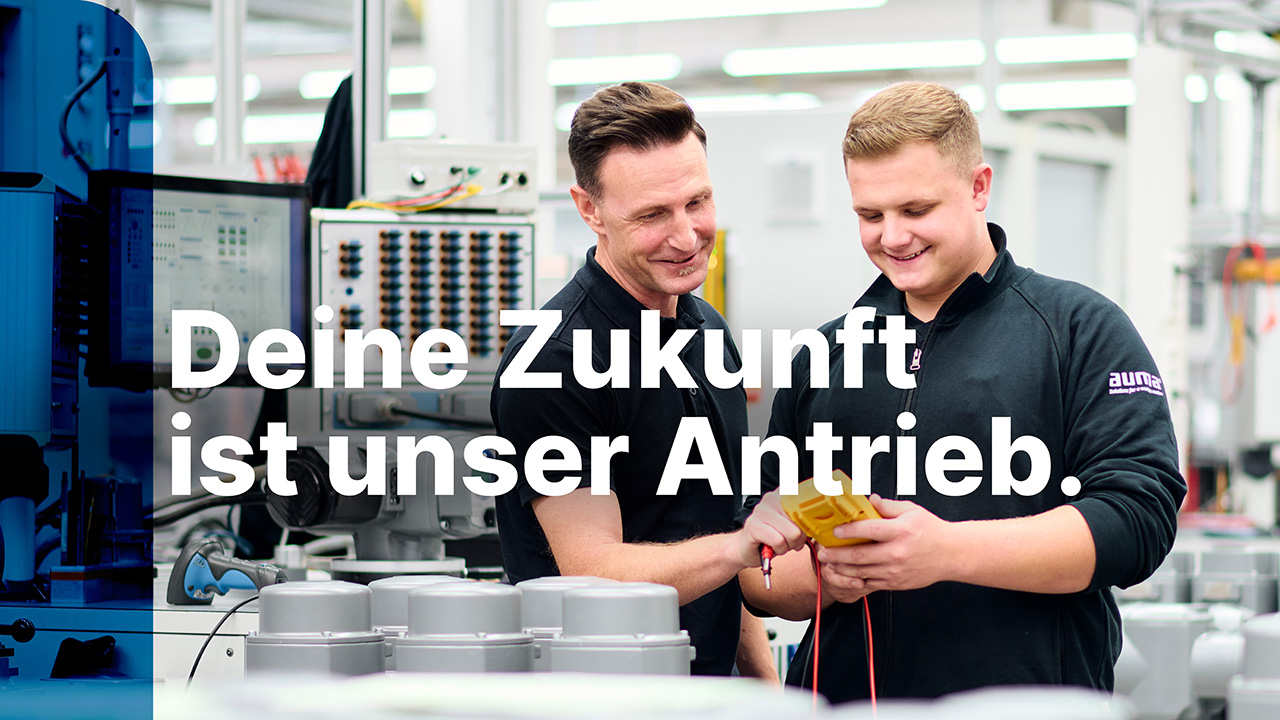 Bild von zwei Männern die sich in der Produktion ein Teil anschauen. Es steht der Spruch auf dem Bild "Deine Zukunft ist unser Antrieb."