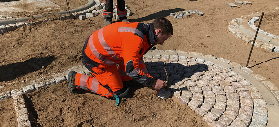 Eine Person verlegt in einem Sandbett Pflastersteine.