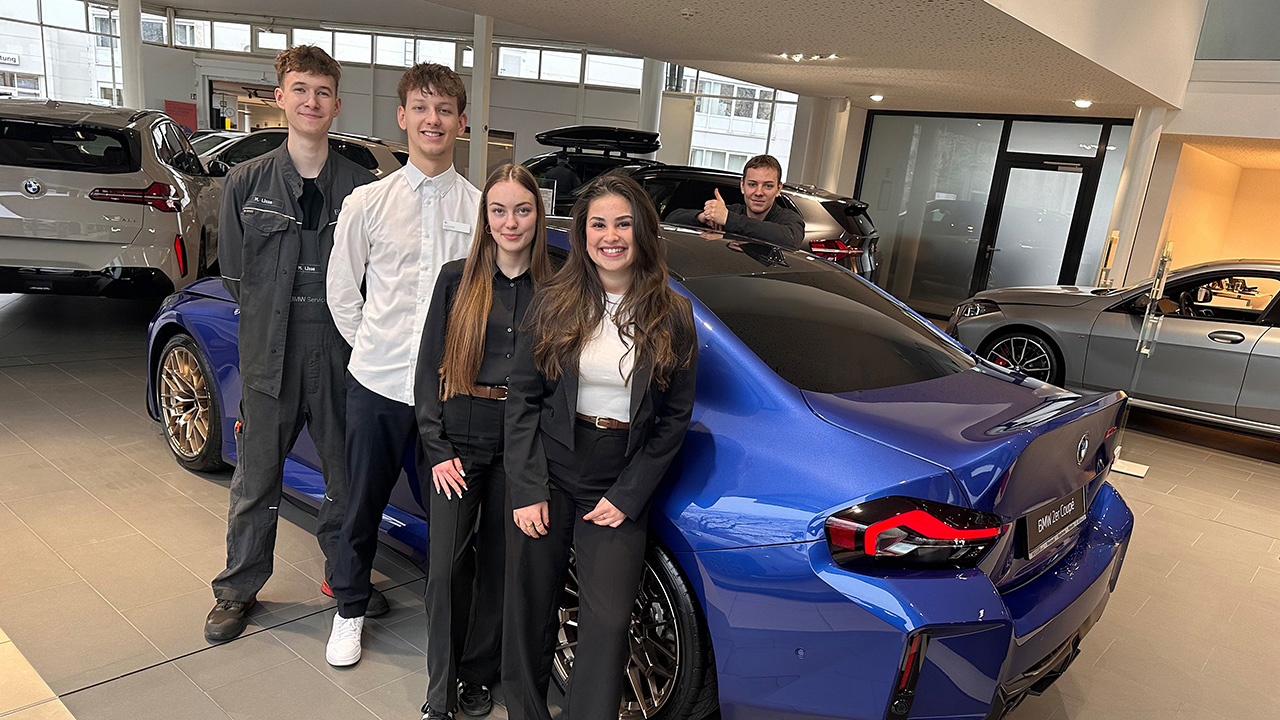 Fünf Personen stehen um ein blaues Auto herum.