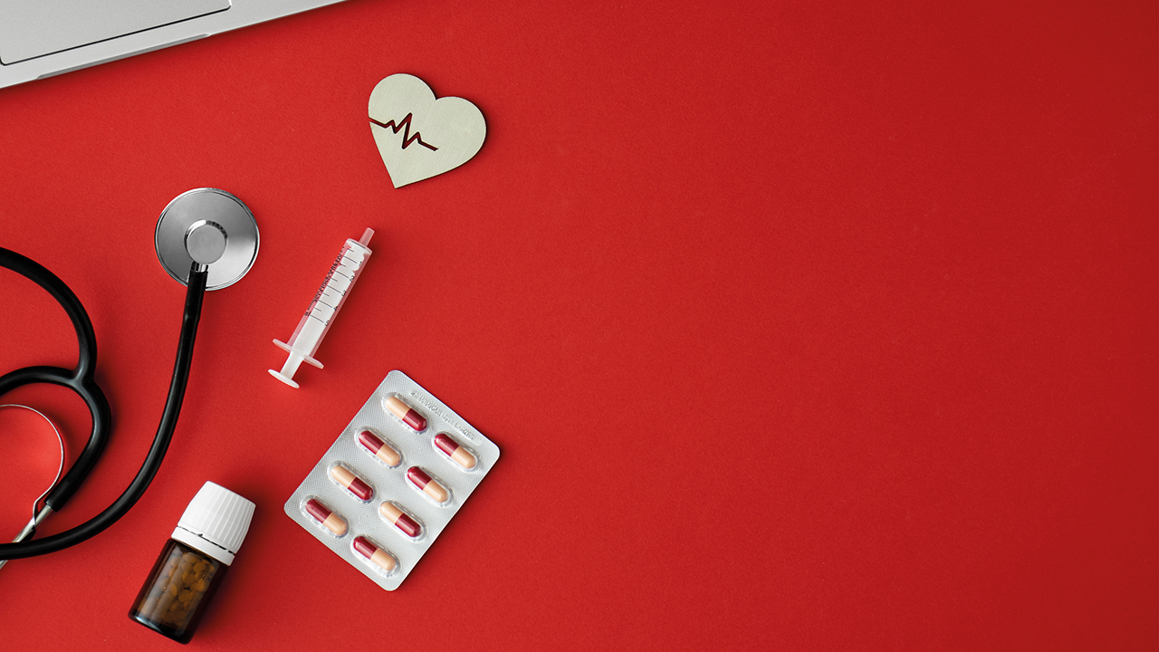 Roter Hintergrund auf dem medizinische Utensilien verteilt liegen mit einem kleinen hölzernen Herz