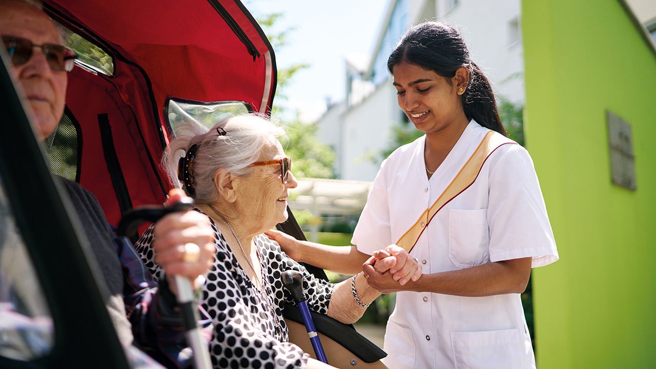 Auf dem Bild sind zwei ältere Personen und eine jüngere zu sehen. Alle lächeln. 