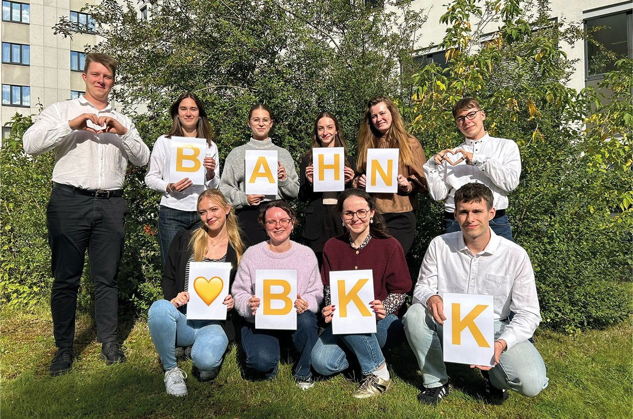 Gruppenbild im Freien, jede Person hält ein Blatt Papier mit einem gelben Buchstaben hoch. Zusammen ergibt es: Bahn BKK