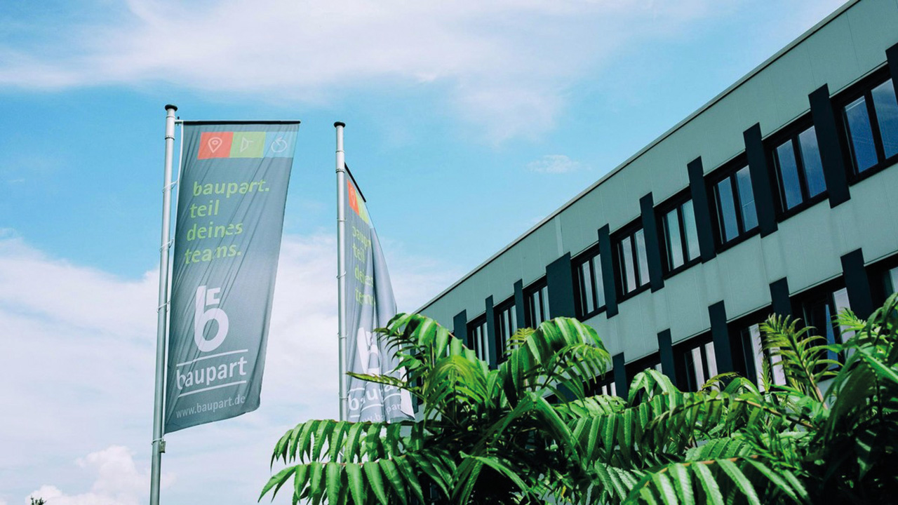 Gebäude vor blauem Himmel, Flagge vor dem Gebäude mit Aufschrift "Baupart - Teil deines Teams"