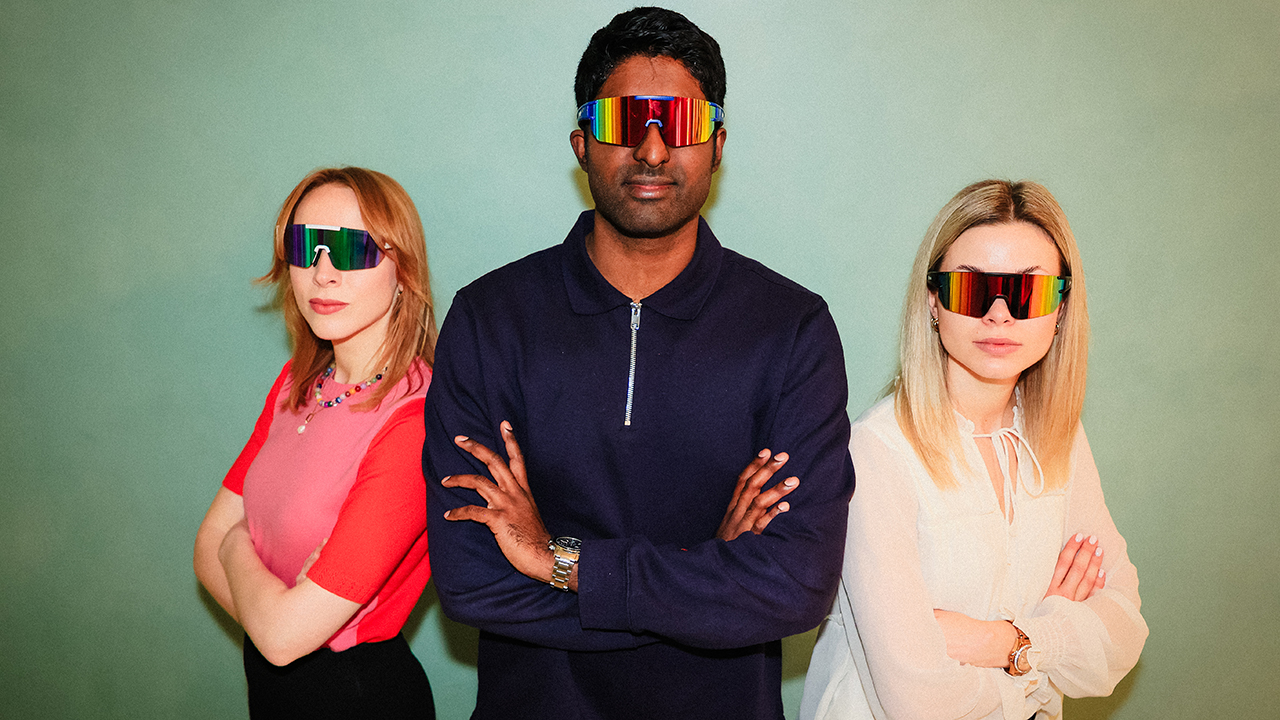 Ein Mann neben dem rechts und links jeweils eine Frau steht. Alle drei haben die Arme verschränkt und tragen futuristische Brillen.