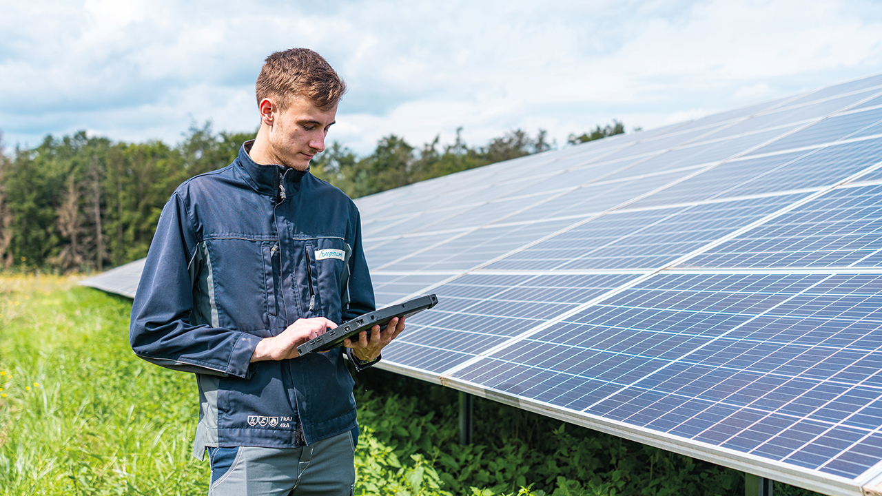 Mitarbeitender mit Tablet in der Hand vor Solarfeld