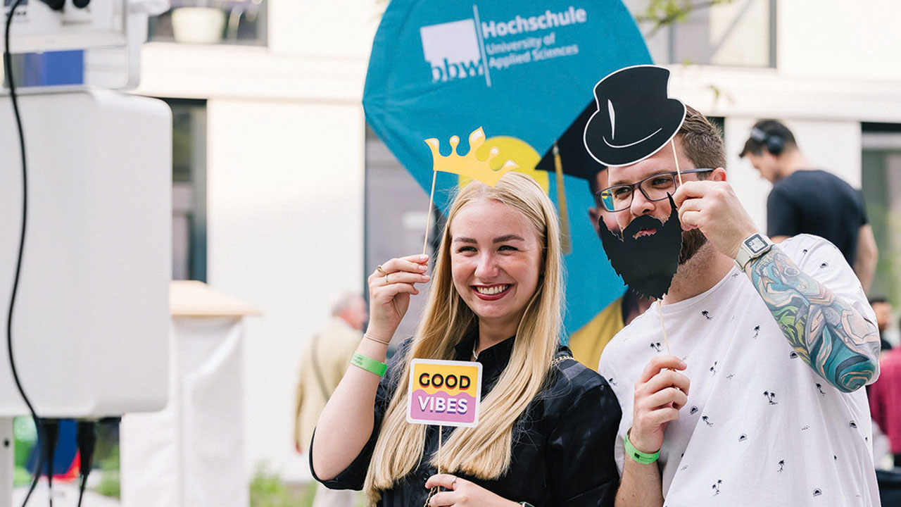 Studierende der bbw Hochschule in der Fotobox mit Krone, Hut und Bart als Accessoires