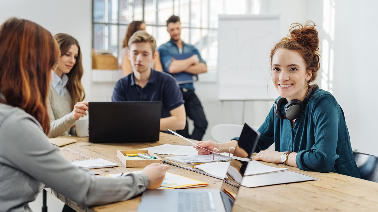 Gruppe junger Mitarbeitender sitzen am Schreibtisch und arbeiten miteinander