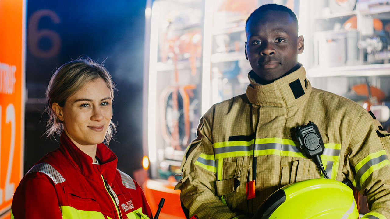 Zwei junge Personen in Feuerwehrbekleidung vor dem Einsatzwagen