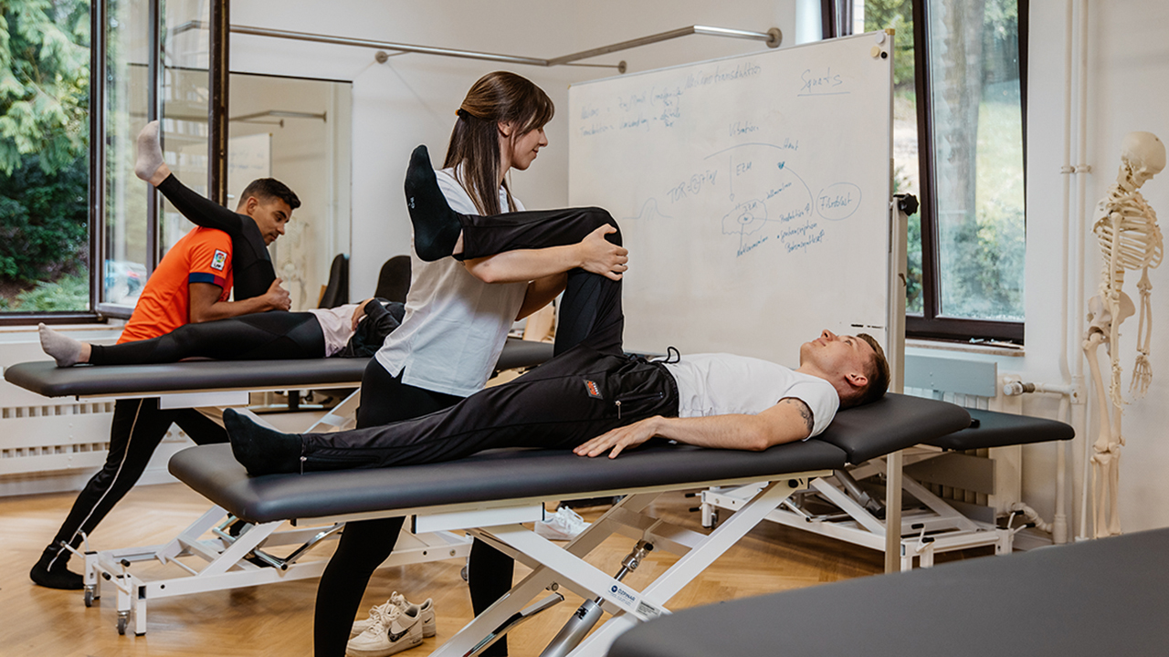 Zwei Physiotherapeut/innen behandeln je einen Menschen auf einem Behandlungstisch.