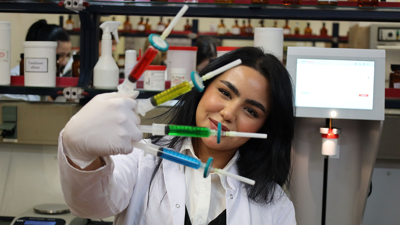 Junge Person hält vier Spritzen in den Farben rot, gelb, grün und blau in der rechten Hand. 
