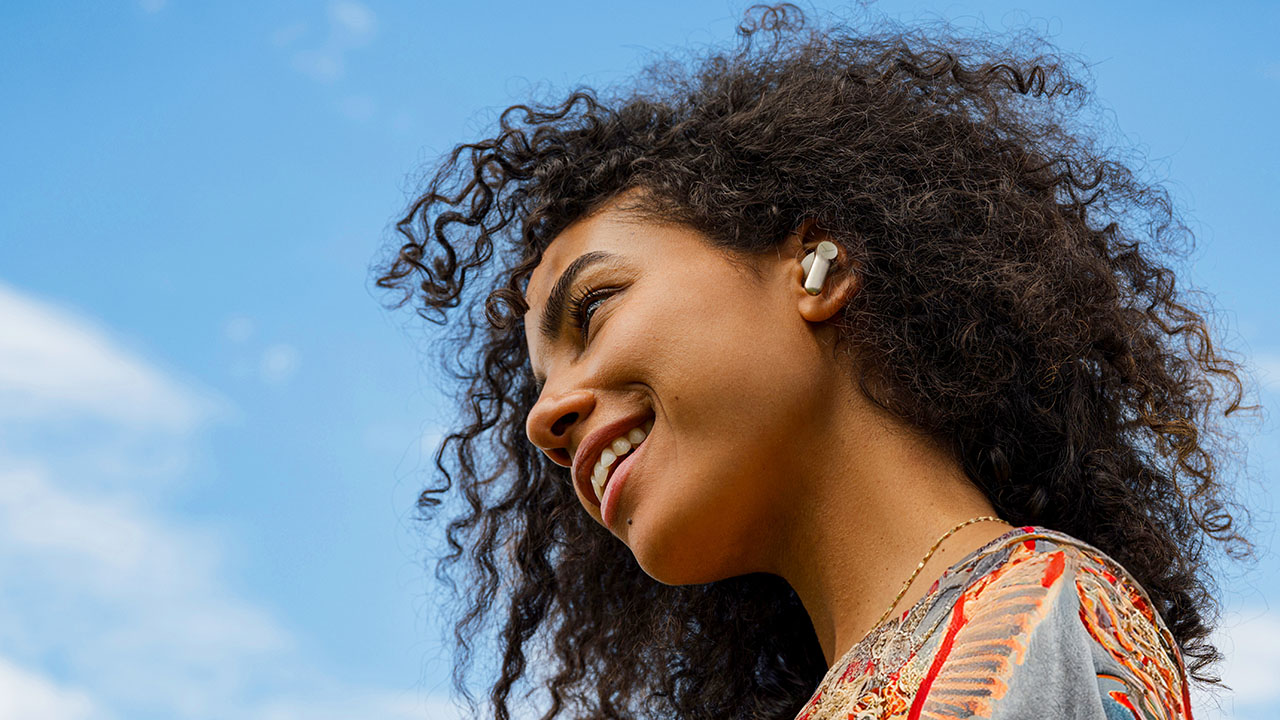 Person steht seitlich zur Kamera lächelt und trägt In-Ear-Kopfhörer.
