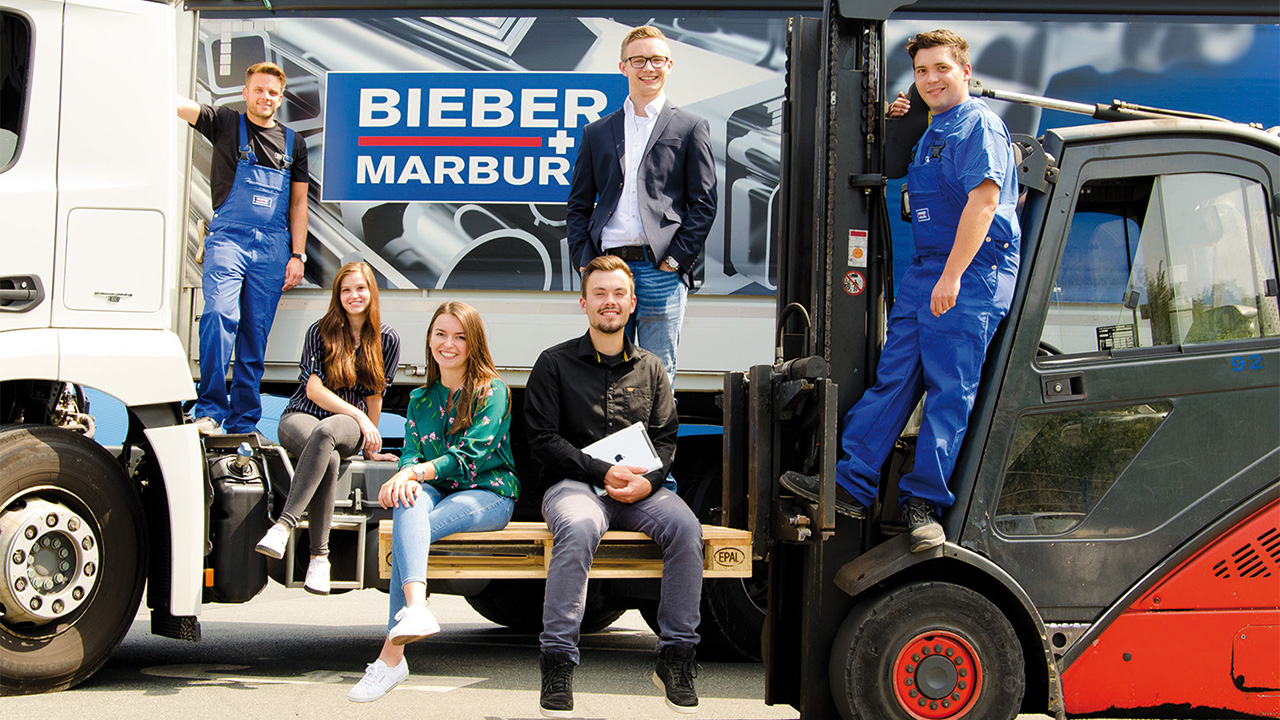 Das Bild zeigt eine Gruppe von Personen die auf einem Radlader sitzt und/oder an einem LKW steht.