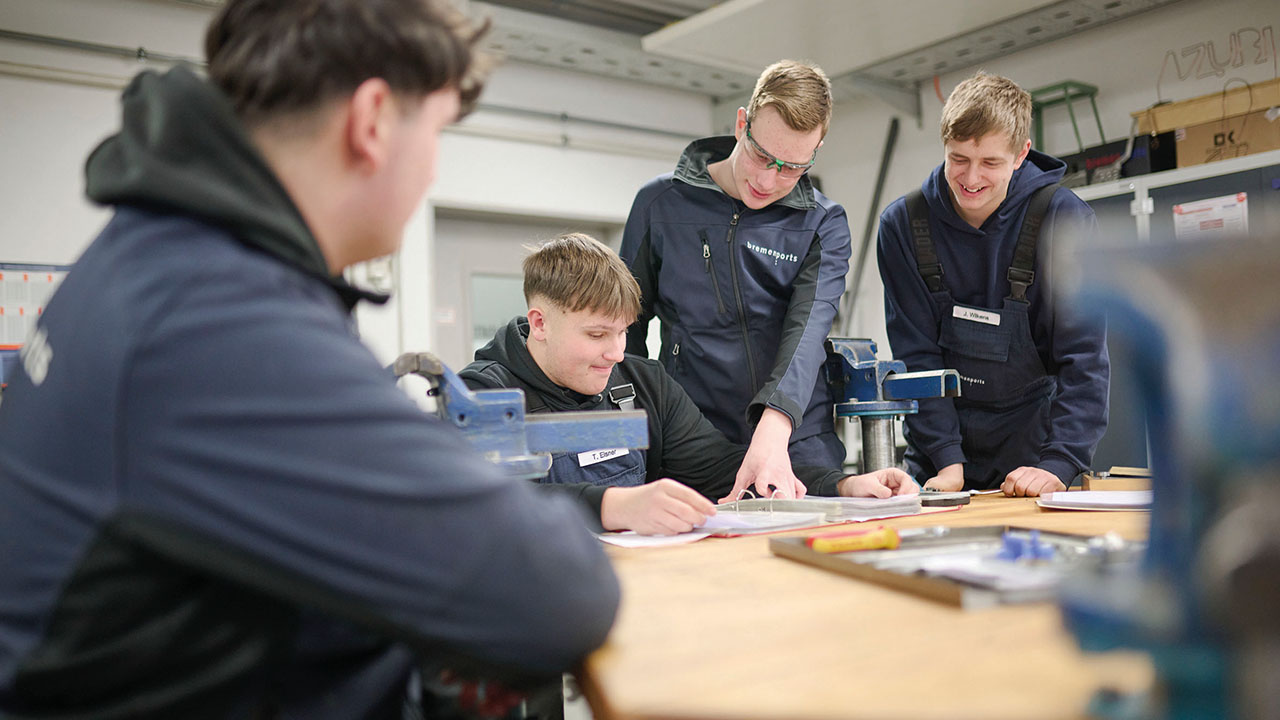 Junge Menschen sitzen in Arbeitskleidung an einem Tisch 