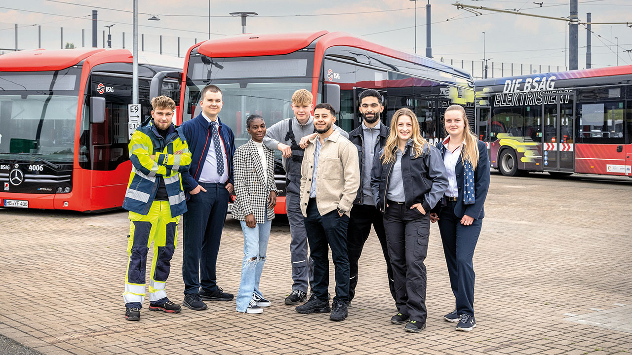 Acht Auszubildende aus verschiedenen Bereichen, im Hintergrund drei Busse der BSAG