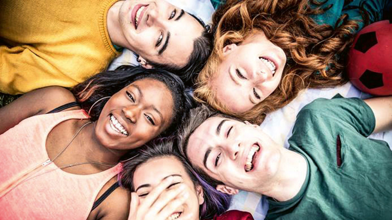 Fünf junge lächelnde Personen liegen im Kreis mit den Köpfen aneinander