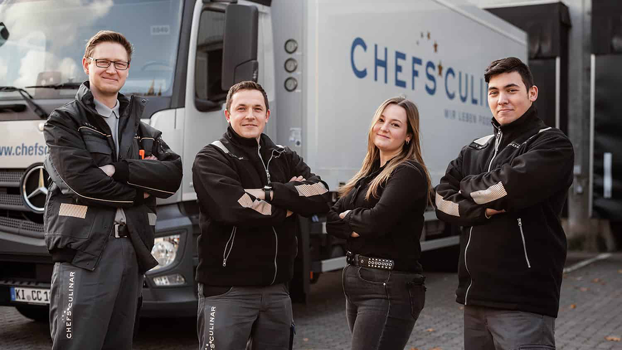 Gruppe von vier Mitarbeitenden stehen vor einem LKW