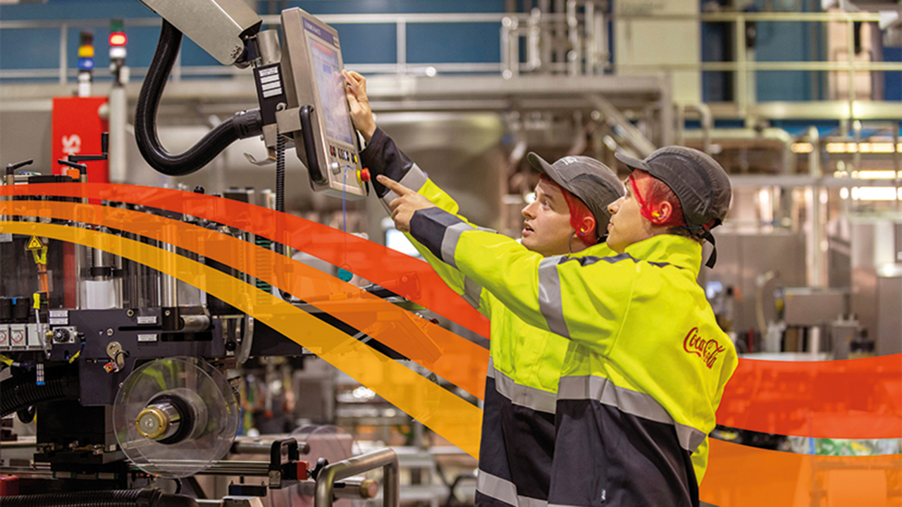 Zwei Mitarbeitende mit Bauhelmen in einer Produktionsstätte bedienen einen Bildschirm einer Maschine