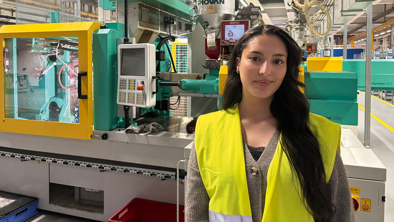 Junge lächelnde Person mit gelber Warnweste in der Produktionshalle