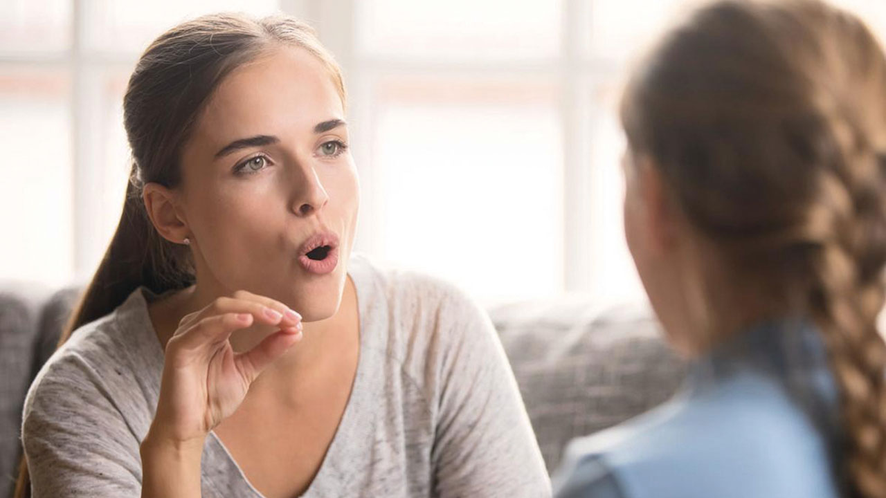 Logopädin formt mit dem Mund ein O für die ihr gegenüber sitzende Patientin