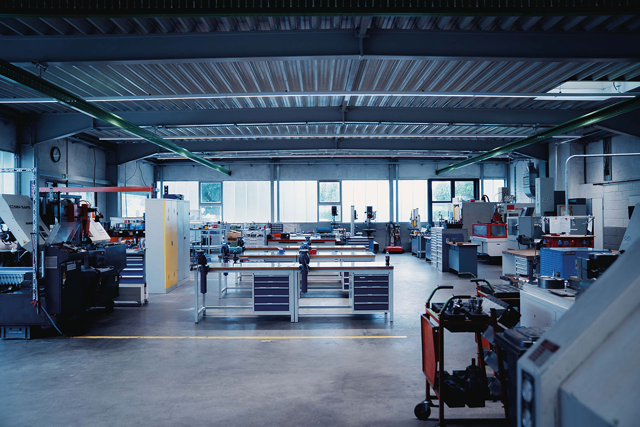 Das Bild zeigt eine große, aufgeräumte Werkhalle mit vielen Werkbänken, Maschinen und Werkzeugen.