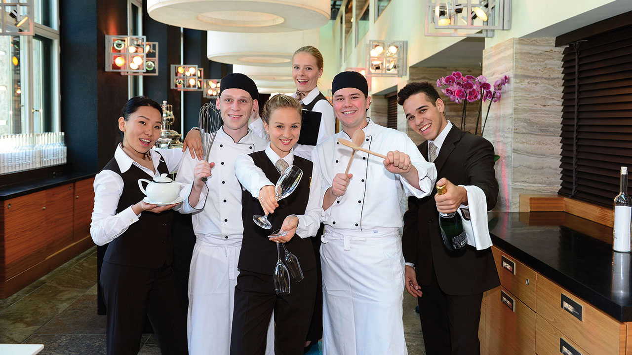 Sechs Auszubildende in Hotel und Gastronomie in entsprechender Arbeitskleidung