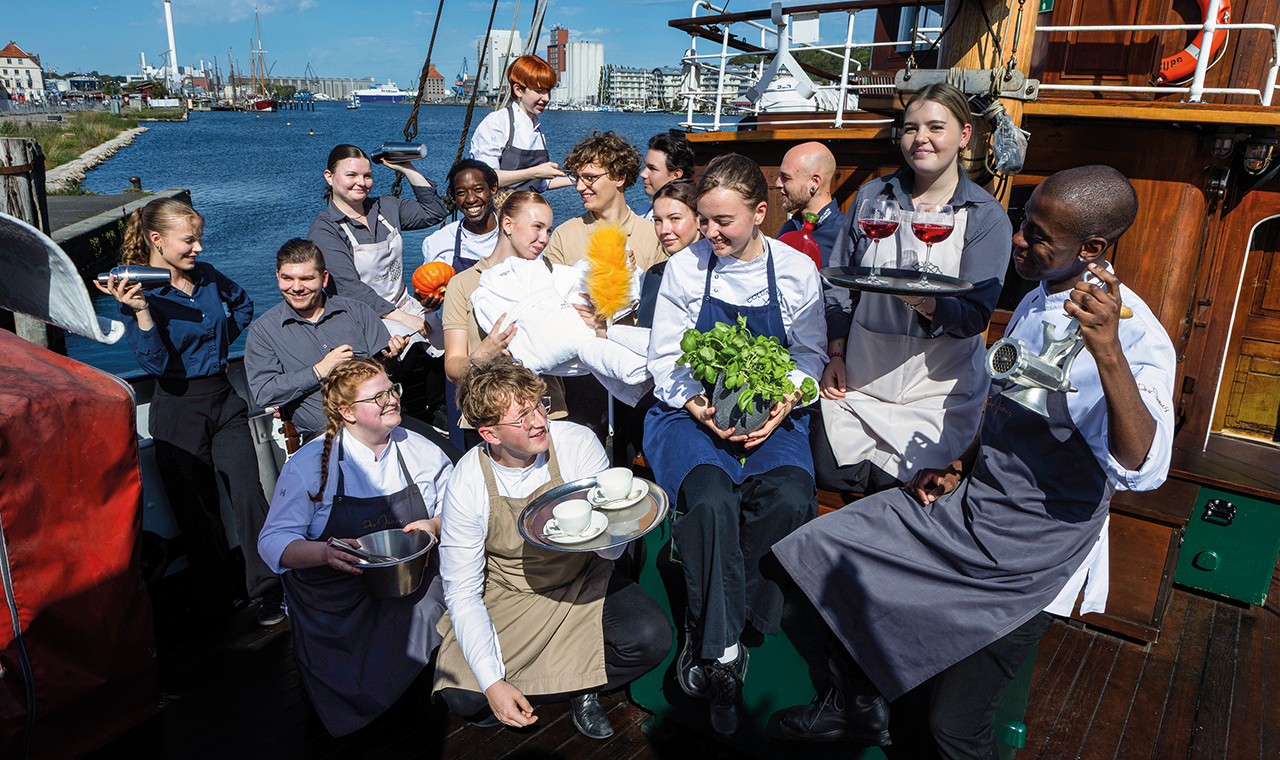 Große Gruppe von Menschen an Bord eines Schiffes, fröhlich, mit Essen und Trinken in den Händen