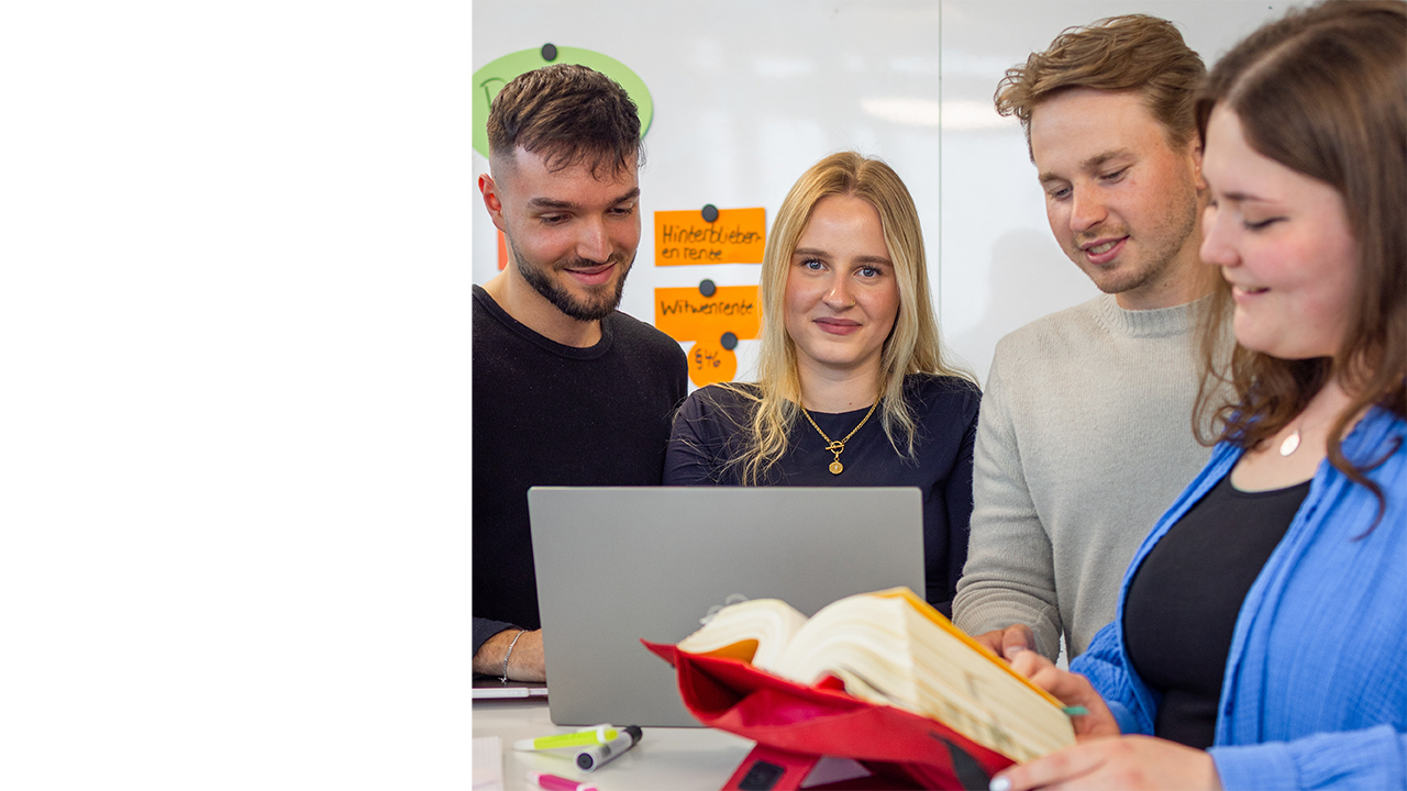 4 Menschen stehen zusammen an einem Laptop und Buch
