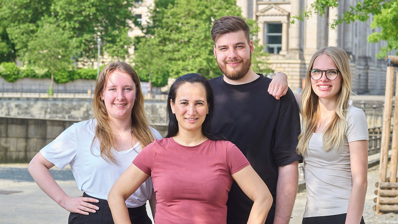 Vier junge lächelnde Menschen vor dem Reichstagsgebäude