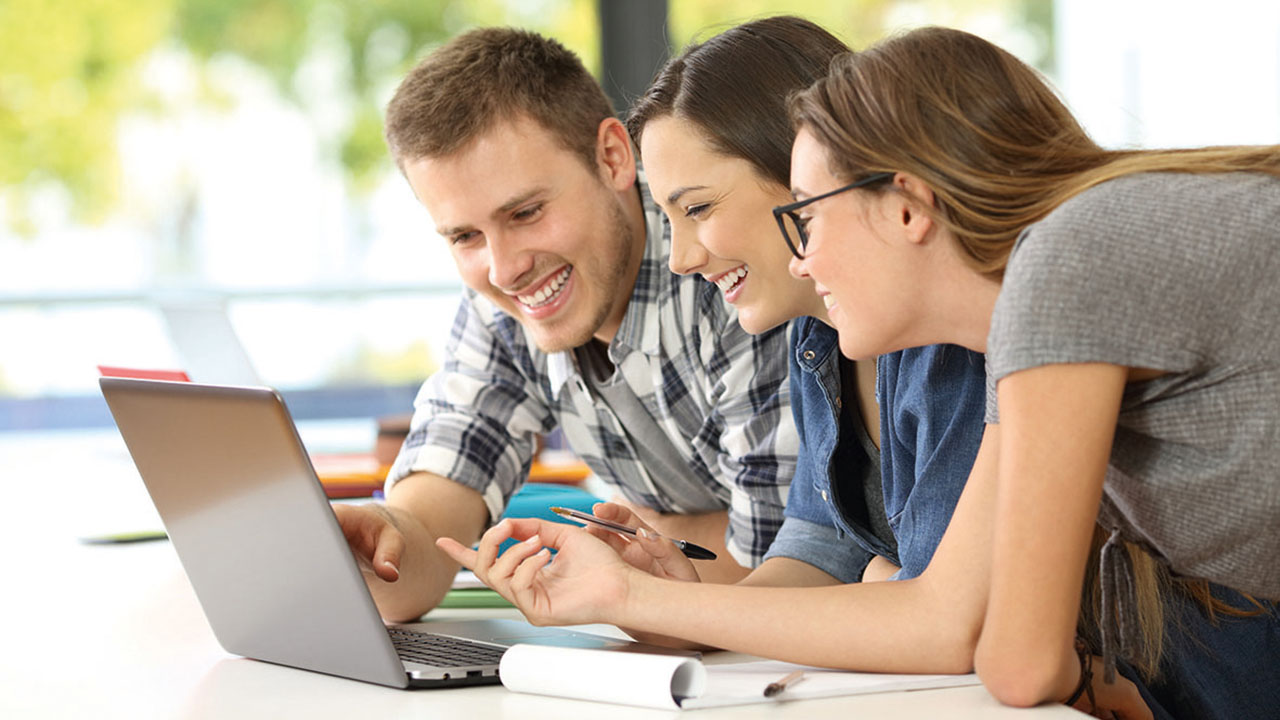 Drei junge lächelnde Personen am Laptop