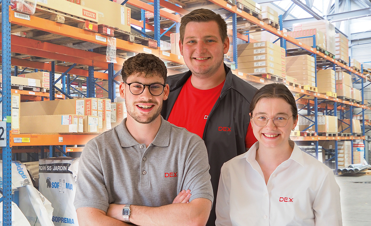 Drei Mitarbeiter/innen in Arbeitskleidung in einer Halle