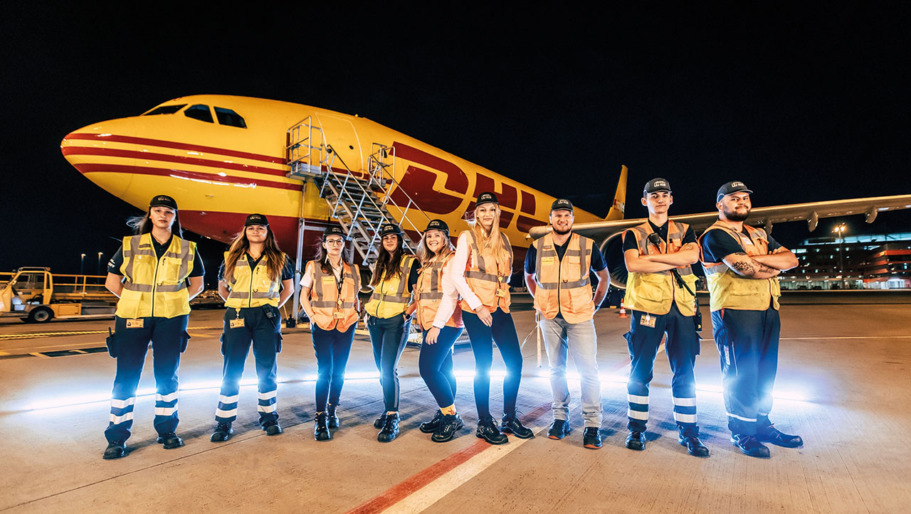 Gruppenbild von DHL-Mitarbeitern unter einem Flugzeug bei Nacht