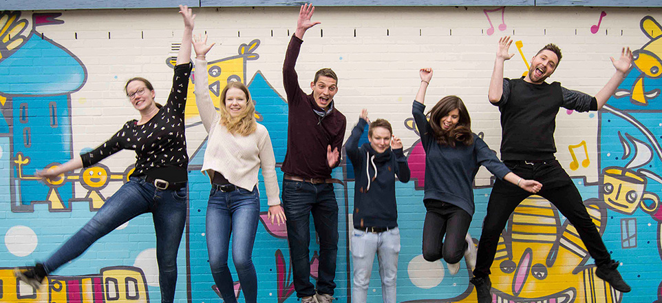 Sechs Menschen springen vor einer bemalten Wand in die Luft