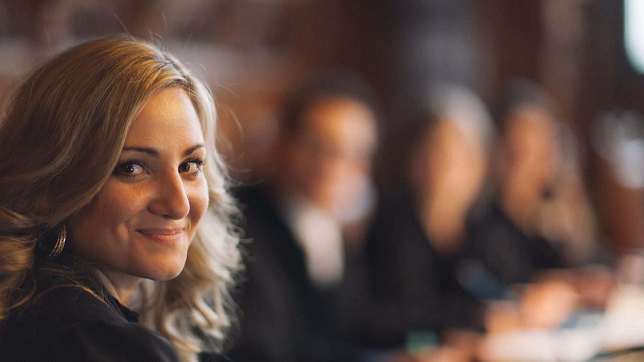 Junge Person lächelt in die Kamera, im Hintergrund verschwommen drei weitere Personen