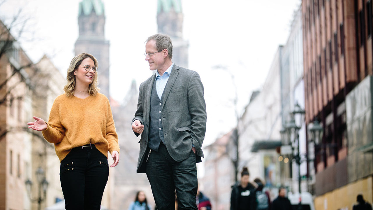 Zwei Personen im Vordergrund, im Hintergrund eine Kirche.
