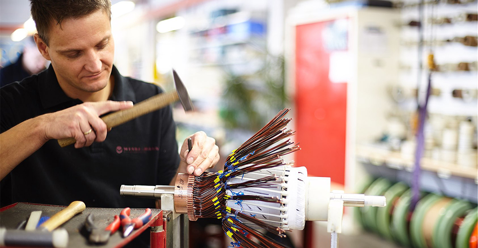 Mann an einer maschine bearbeitet etwas mit einem Hammer