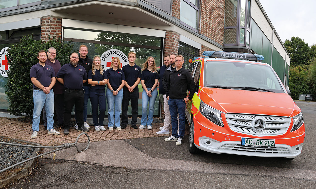 Notfallsanitäter stehen vor einem Haus, daneben ein orangenes Auto