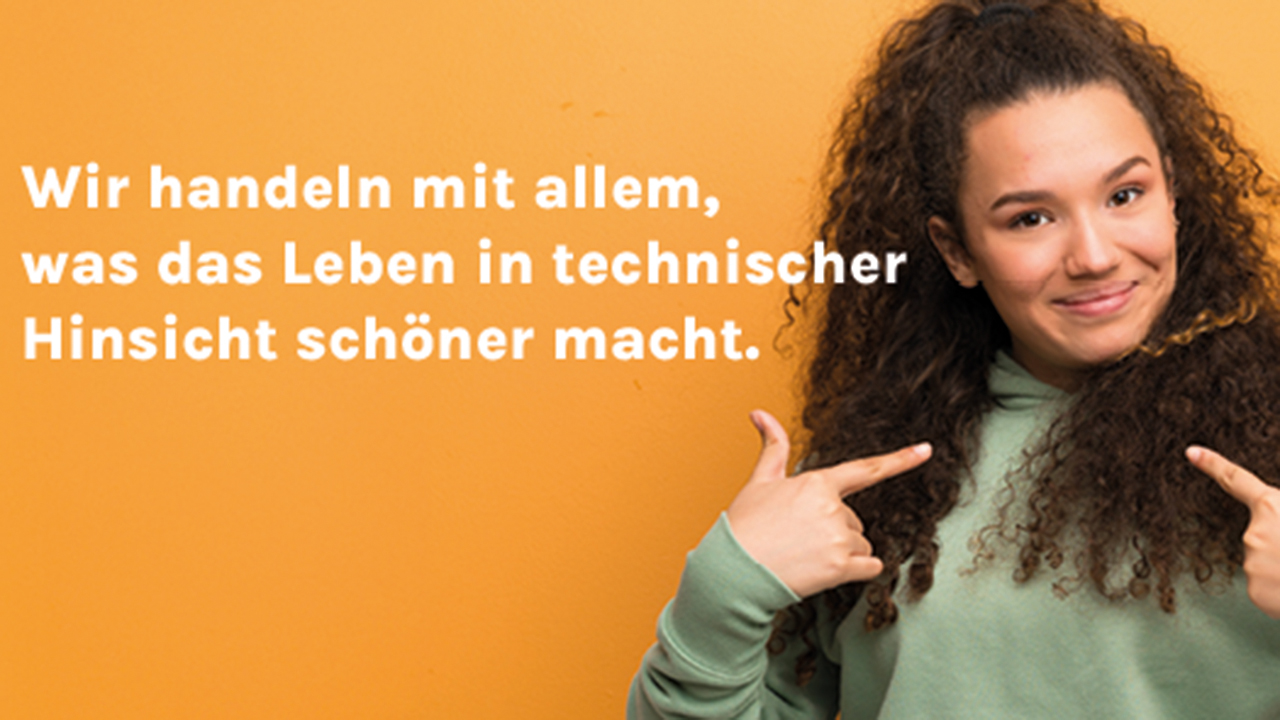 Vor orangefarbenem Hintergrund sieht man auf der rechten Seite eine junge Frau die mit ihren beiden Zeigefingern auf sich zeigt und sich freut. Daneben der Spruch: Wir handeln mit allem, was das Leben in technischer Hinsicht schöner macht.
