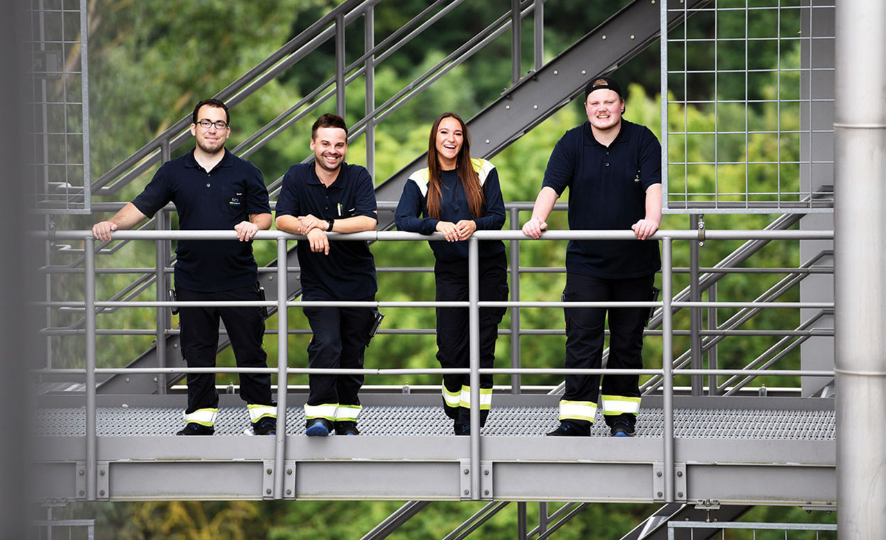 4 junge Menschen in schwarzer Arbeitskleidung auf einem Metallgerüst