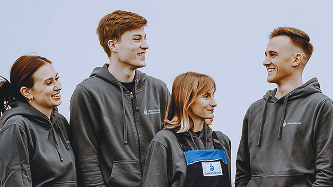 Vier Personen in Arbeitskleidung sehen sich an und lächeln.
